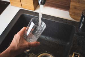 A close-up of a hand filling up a glass of water at the kitchen sink.